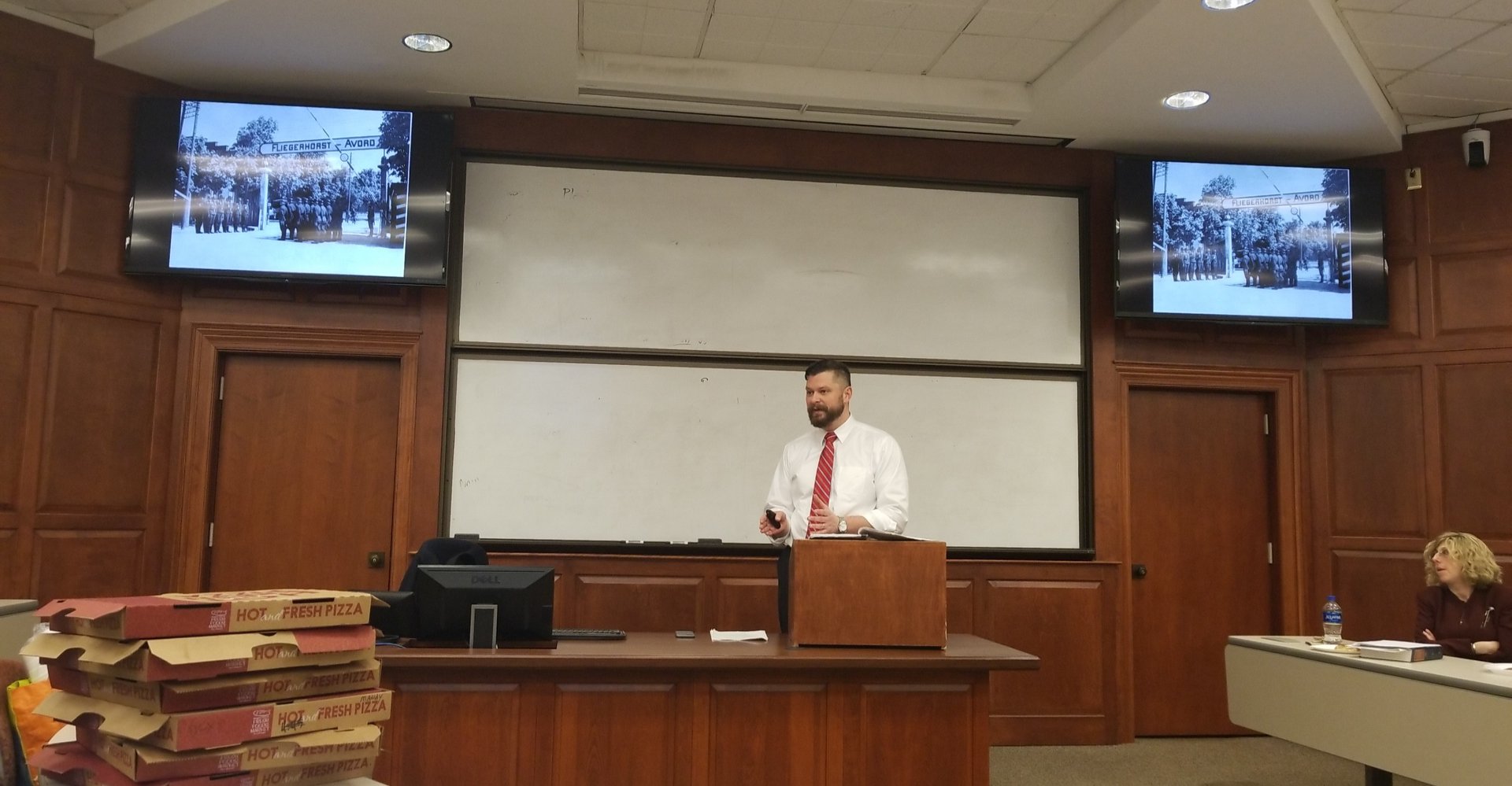 man lecturing from a podium in front of two projectors