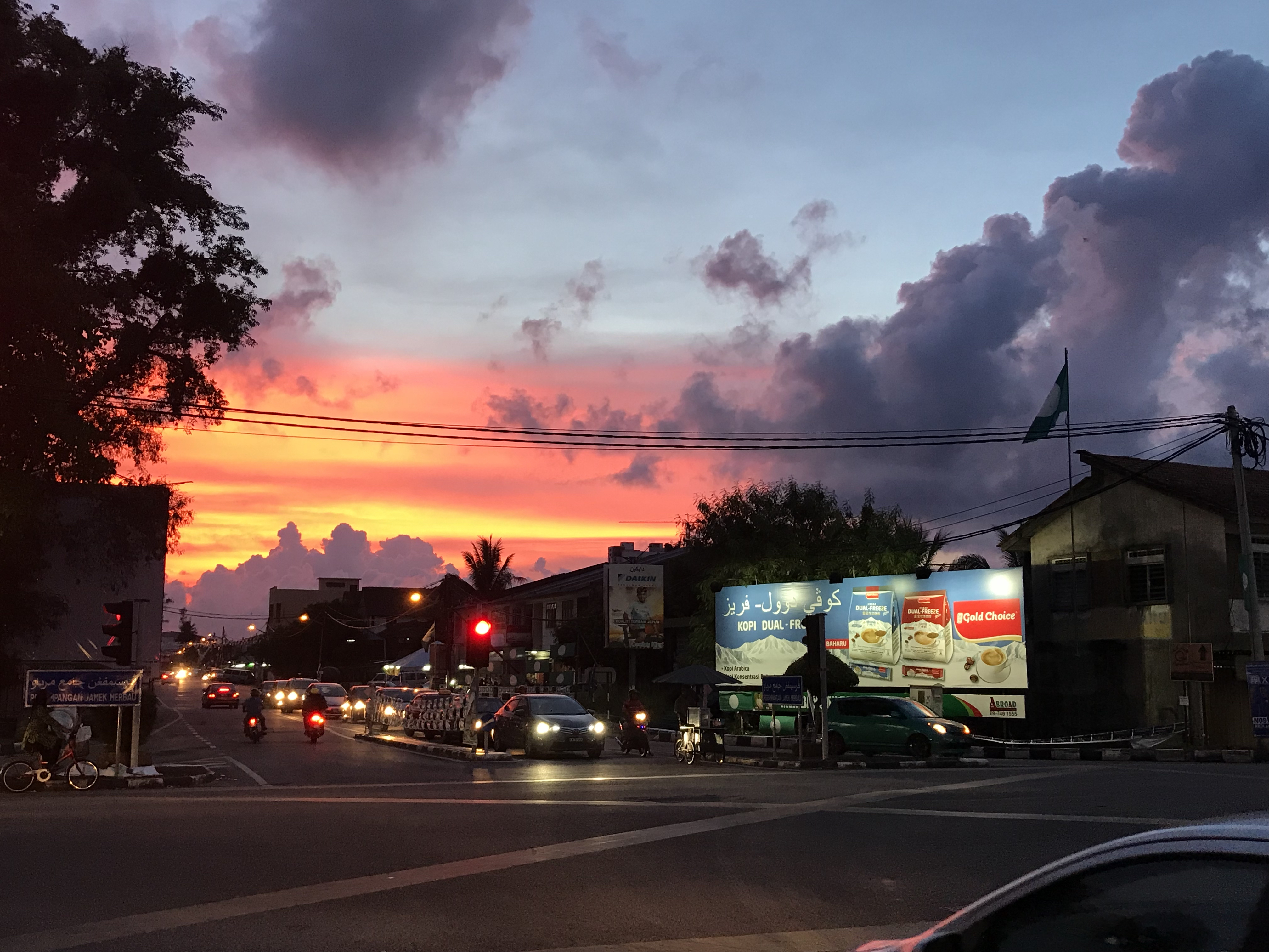 A flag flies over a busy intersection in Kota Bharu, Malaysia as the sun sets.
