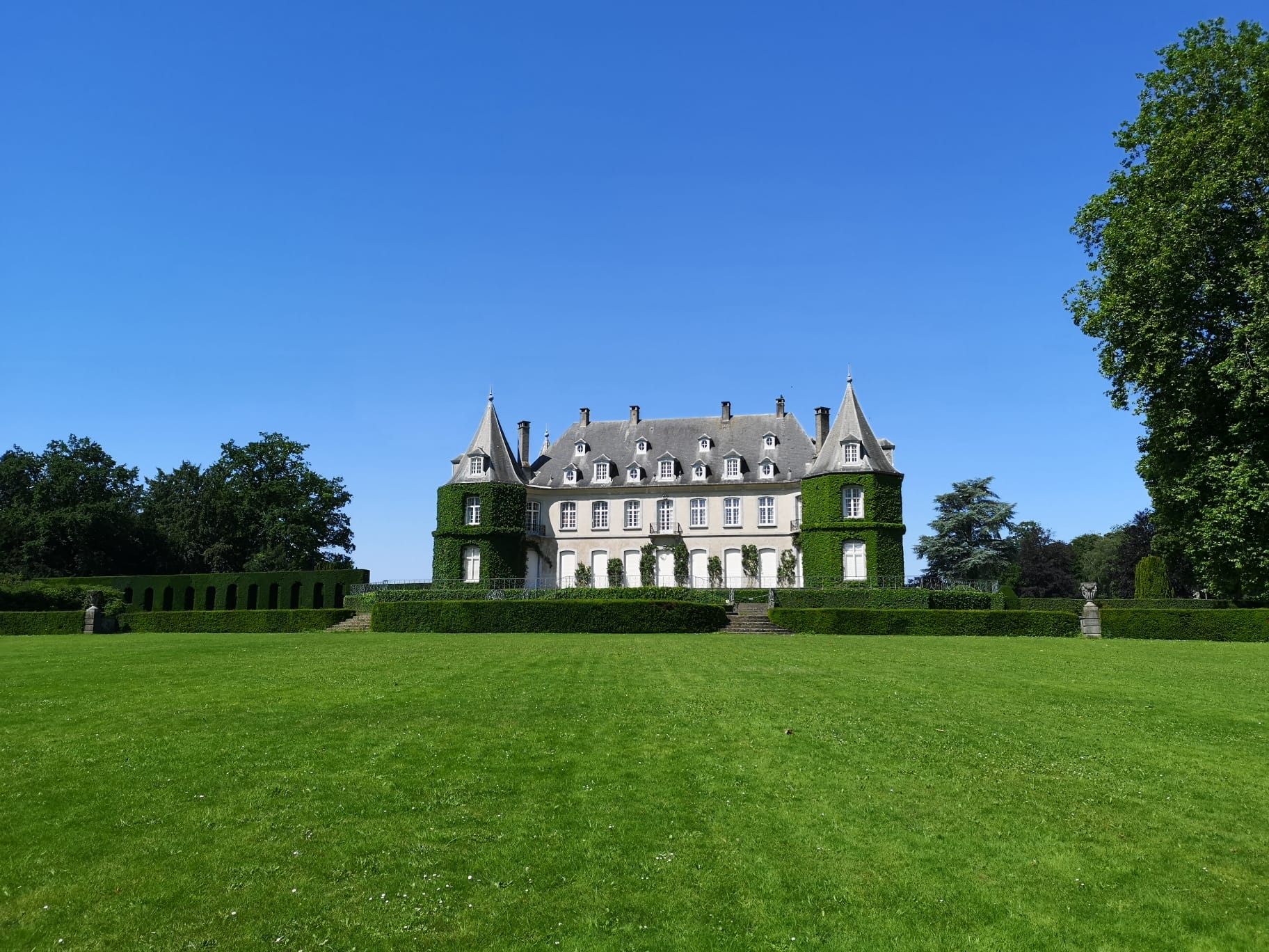 Chateau de La Hulpe with a large green grass space in front and a blue sky behind.