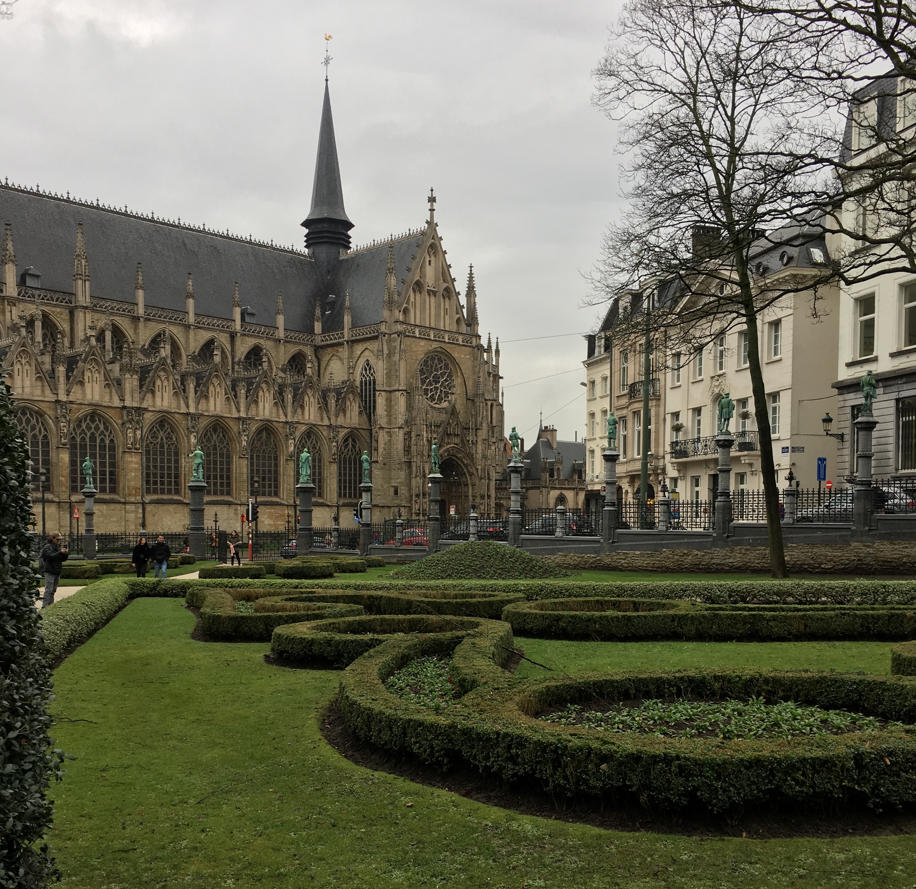 The Notre Dame Church of Sablon on a cloudy day, with a green garden in the foreground