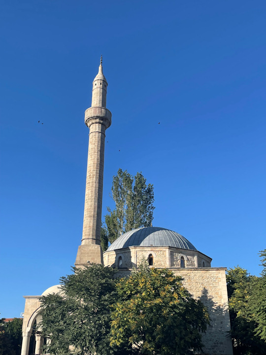 The light blue dome and stone minaret of a mosque against clear blue sky.