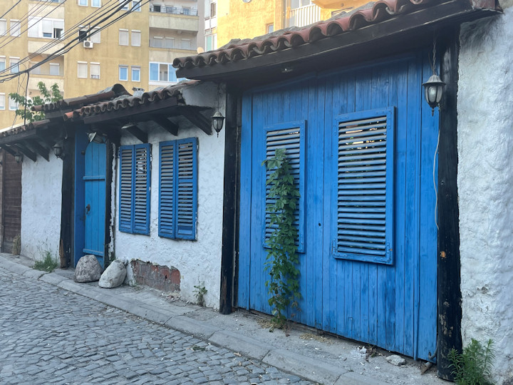 A blue gate, door, and shingles in an old white wall on a cobblestone street.