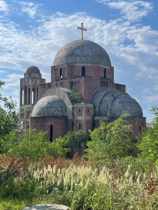 The brick structure and domes of an unfinished Serbian Orthodox church topped with a golden cross.