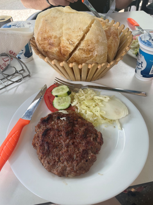 A spiced grilled meat patty served with fresh vegetables and warm bread.